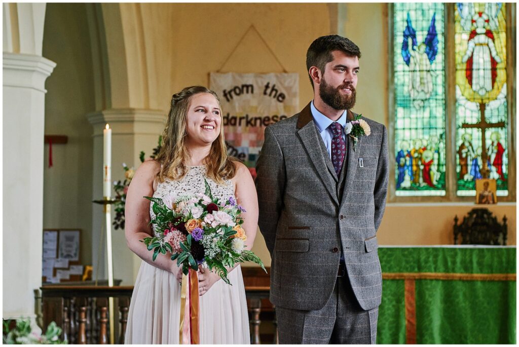 Bride and groom smiling whilst stood in church at their wedding in Essex