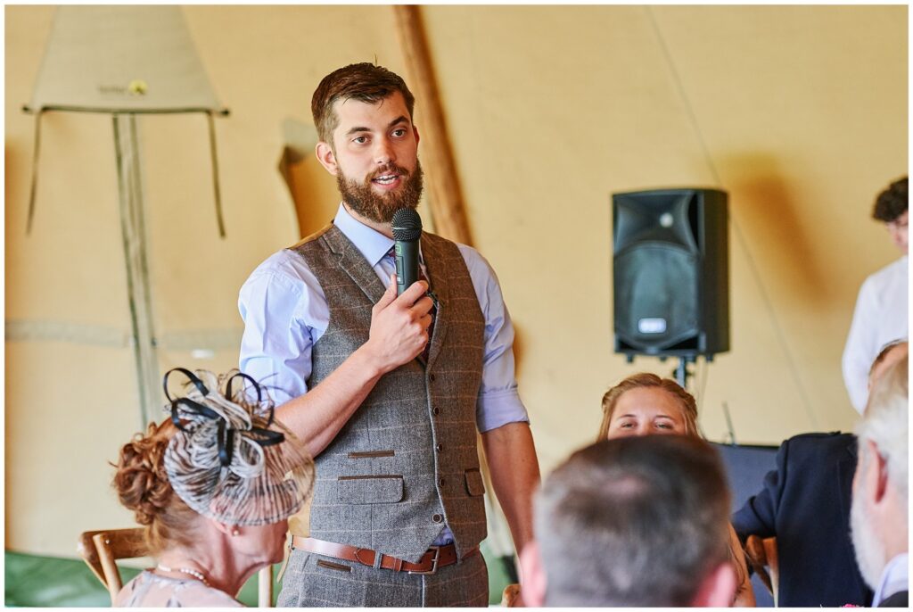 relaxed groom giving a speech inside a festival tipi tent in Essex