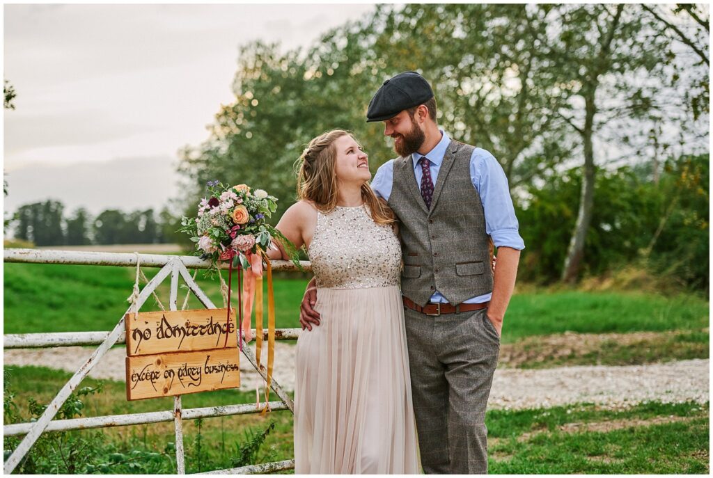 Bride and groom stood in a field smiling next to a farm gate