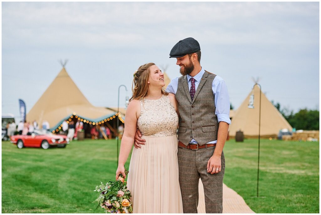 Happy bride and groom stood in front of thier festival tipi wedding tent