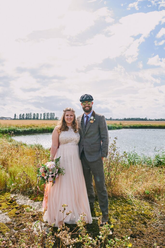 relaxed bride and groom smiling in front of a lake in Essex