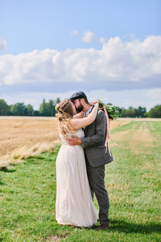 Bride and groom kissing whilst stood in a field in Essex