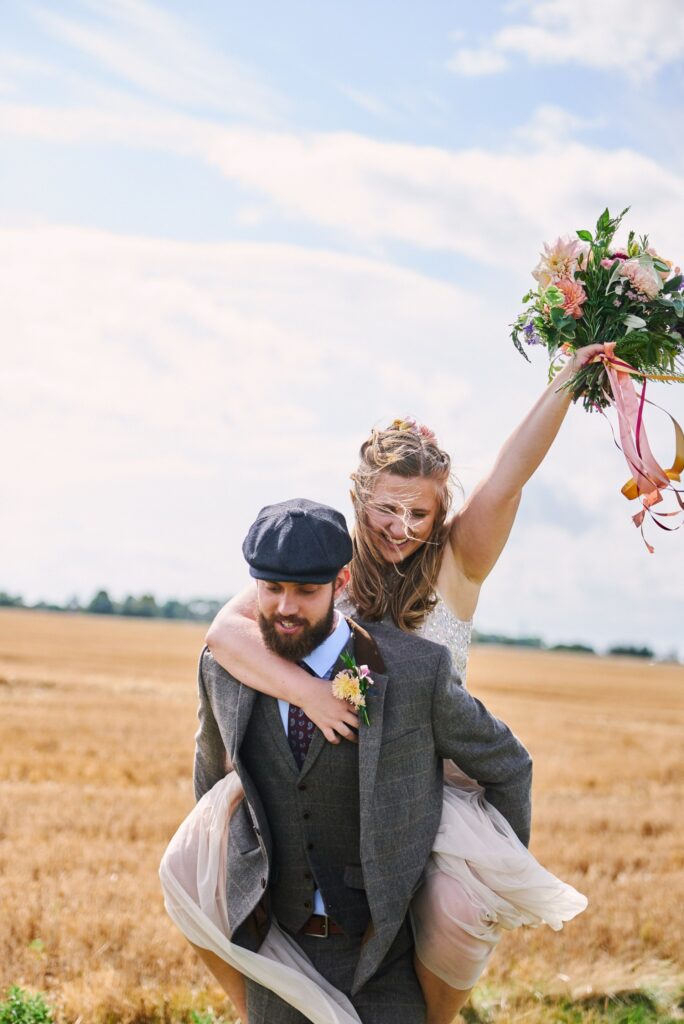 Bride getting a piggy back from her groom during summer wedding in Essex
