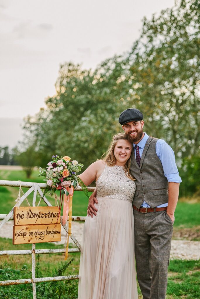 Bride and groom stood in a field smiling next to a farm gate