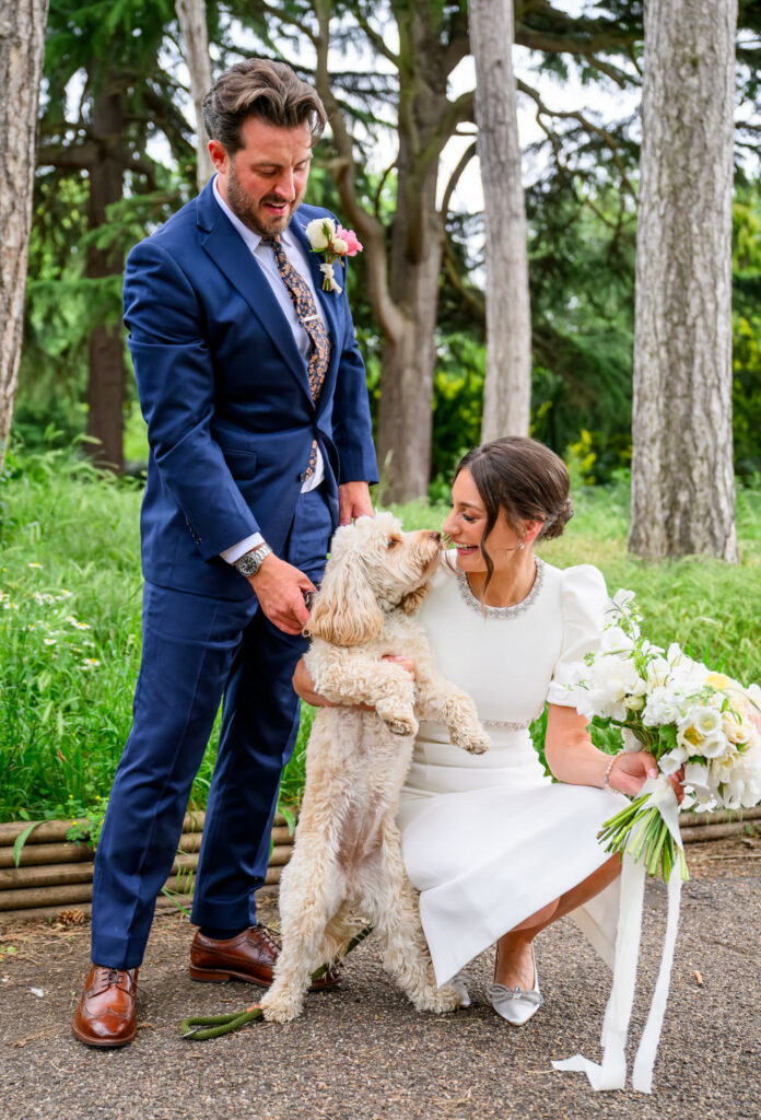 Bride and groom playing with their dog during wedding photos in front of trees