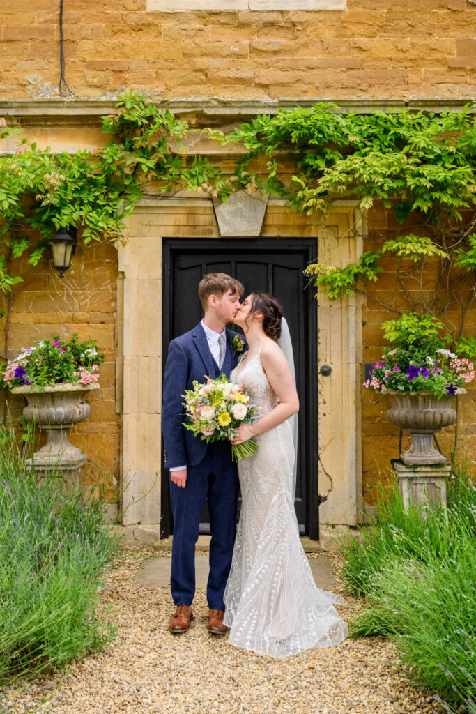 Bride and groom kissing in front of the ivy-covered manor doorway