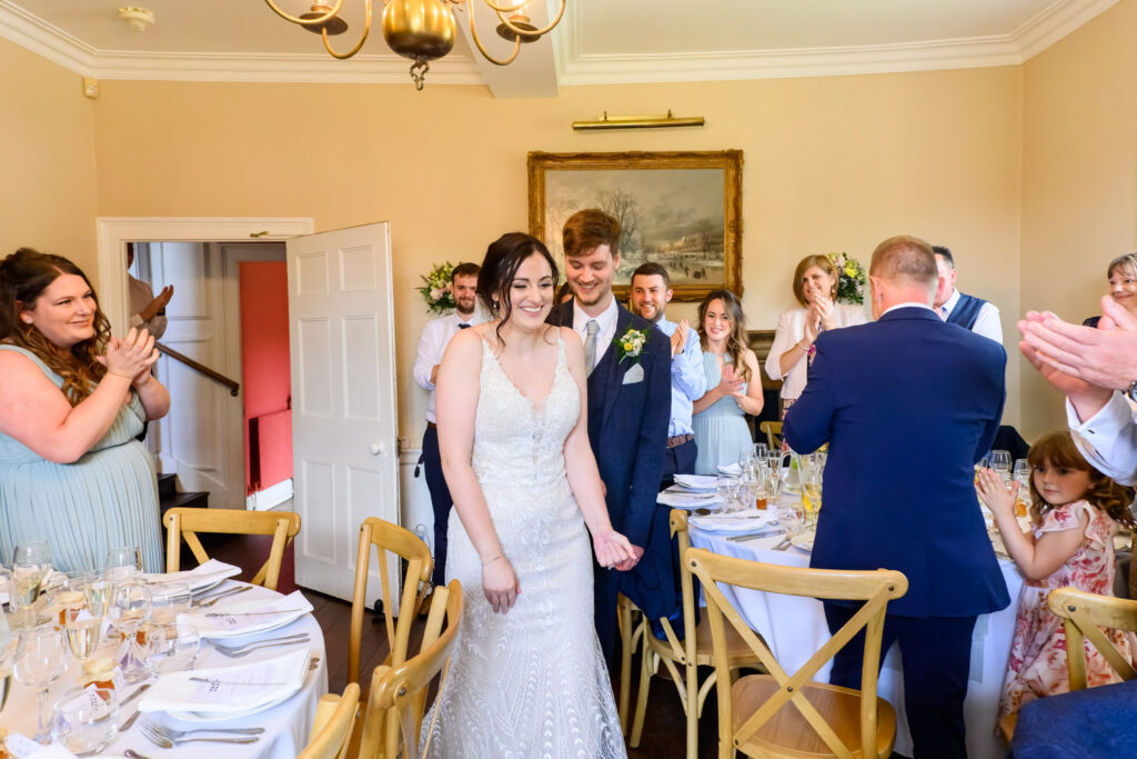 Bride and groom entering the wedding breakfast to applause from guests
