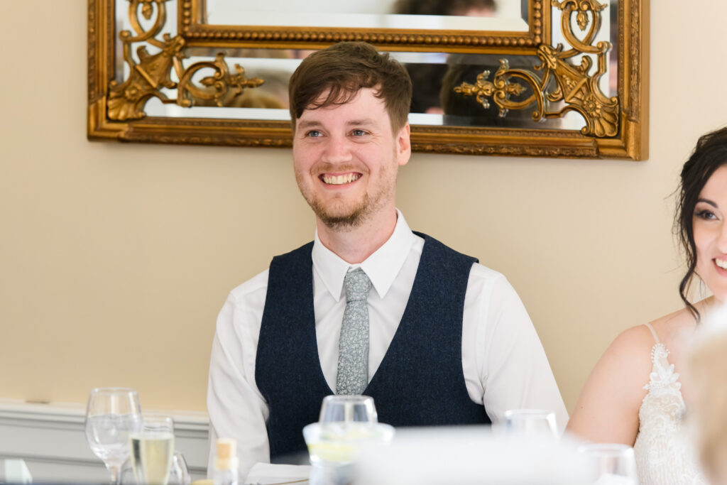 Groom smiling during wedding speeches at the reception table