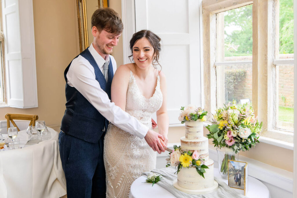 Bride and groom cutting their wedding cake together beside the window