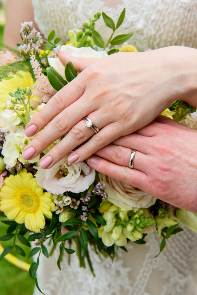 Close-up of bride and groom holding hands showing wedding rings