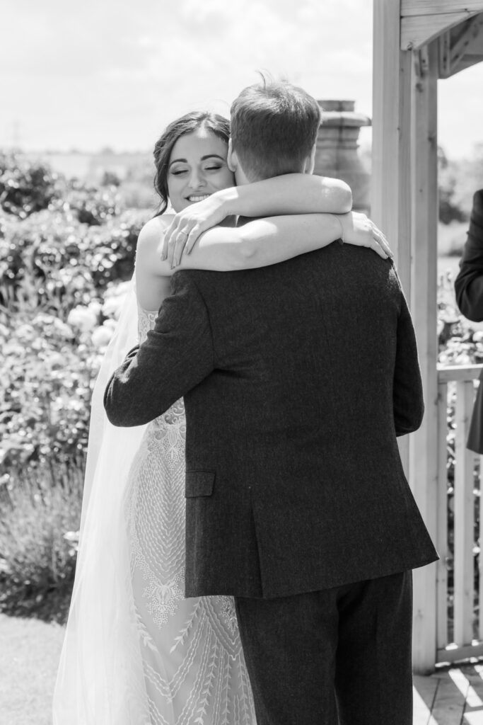 Black and white photo of bride hugging groom after outdoor wedding ceremony at Allington Manor