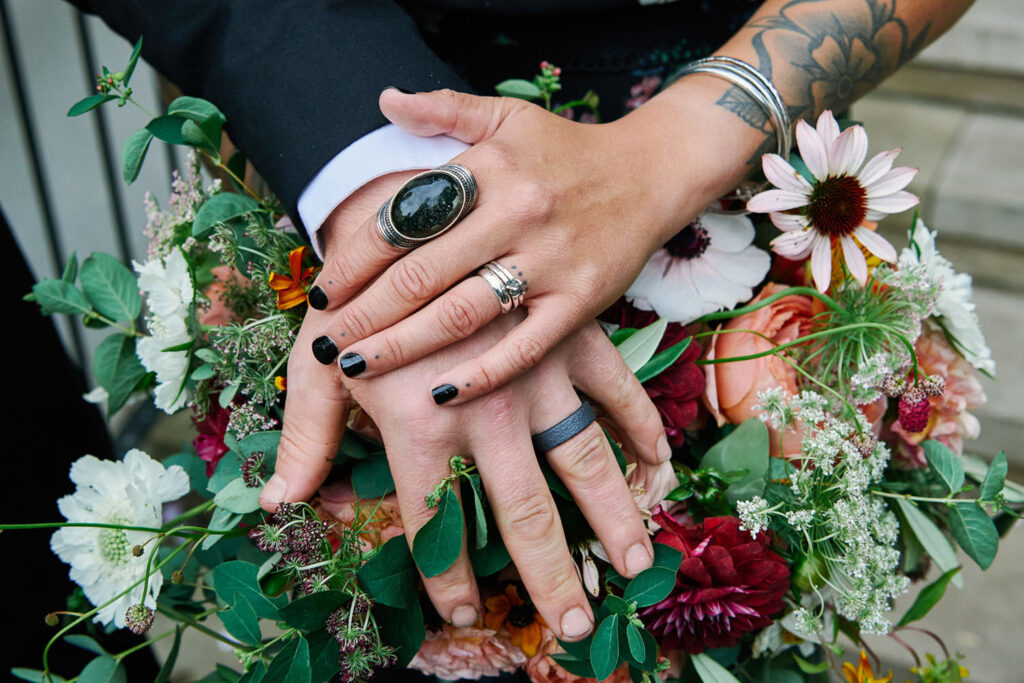 tattooed bride and groom hands with Wedding rings resting on flowers