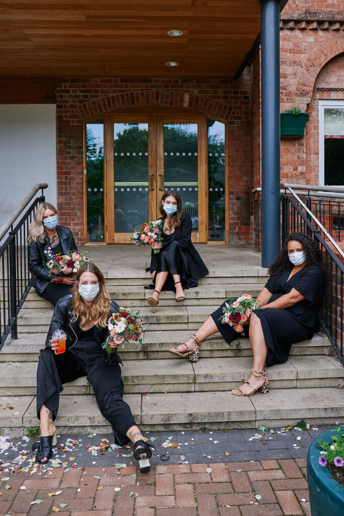 Bridesmaids sitting on steps wearing masks 