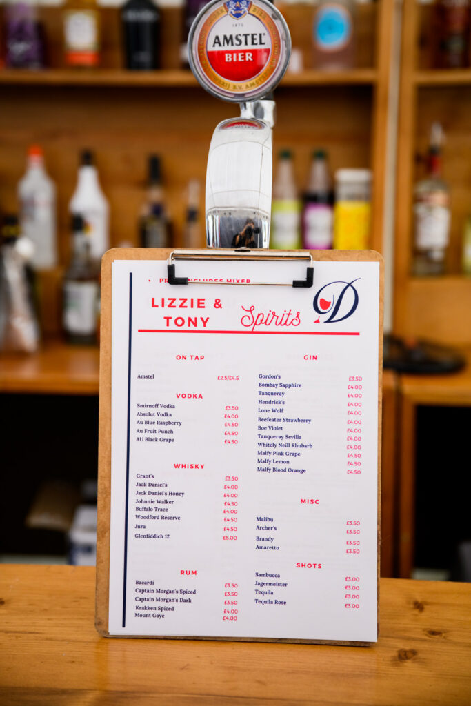 Custom wedding bar drinks menu displayed on counter during evening reception at countryside venue