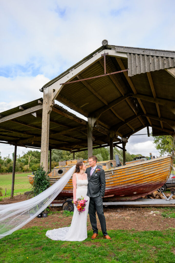 Bride and groom portrait by rustic boat at Willow Marsh Farm wedding venue