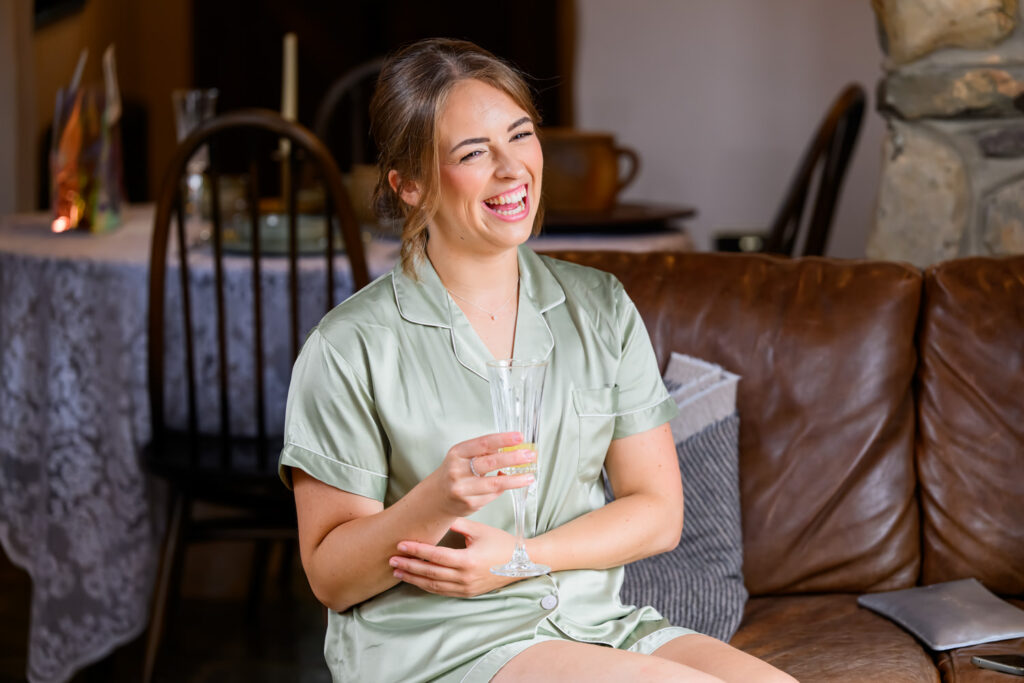 Bridesmaid in sage green robe laughing during bridal prep at Willow Marsh Farm wedding
