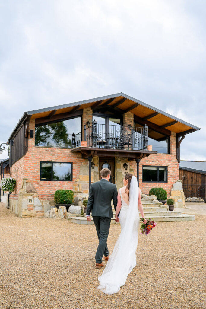 Bride and groom walking toward rustic countryside wedding venue