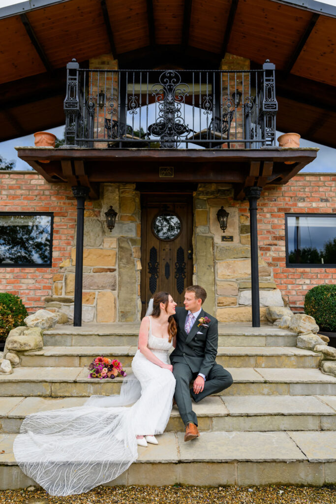 Bride and groom sitting on stone steps outside Willow Marsh Farm wedding venue