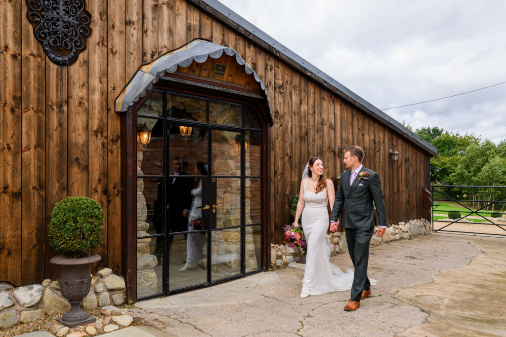 Bride and groom walking past barn entrance at Willow Marsh Farm wedding venue