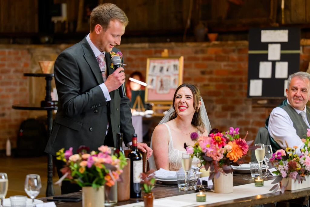 Groom giving speech while bride smiles at the top table