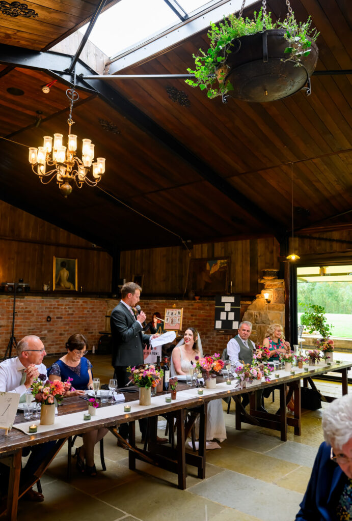 Groom giving speech at top table during barn wedding reception