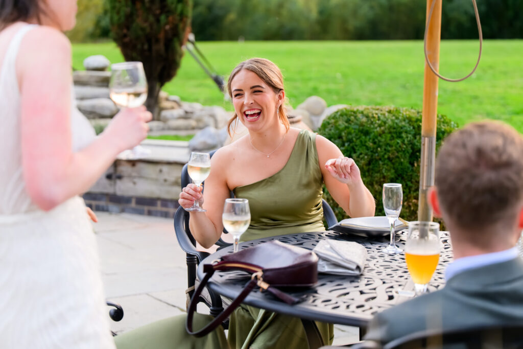 Wedding guest laughing while holding glass of wine during evening reception