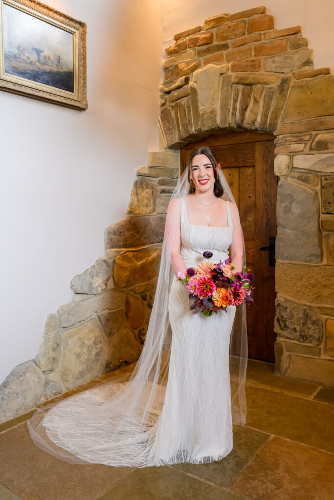 Bride holding colourful bouquet in front of stone doorway before the ceremony
