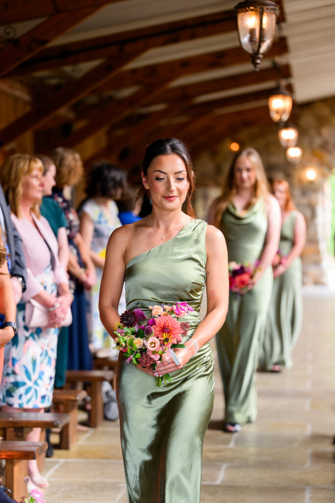 Bridesmaid in sage green dress walking down the aisle during rustic barn wedding ceremony