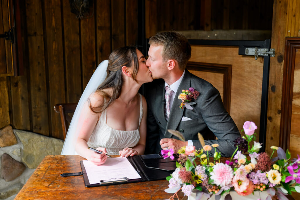 Bride and groom kissing while signing the wedding register after ceremony