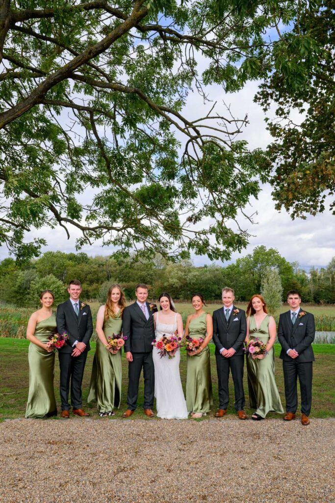 Bride and groom with bridesmaids and groomsmen in sage green dresses during group portraits