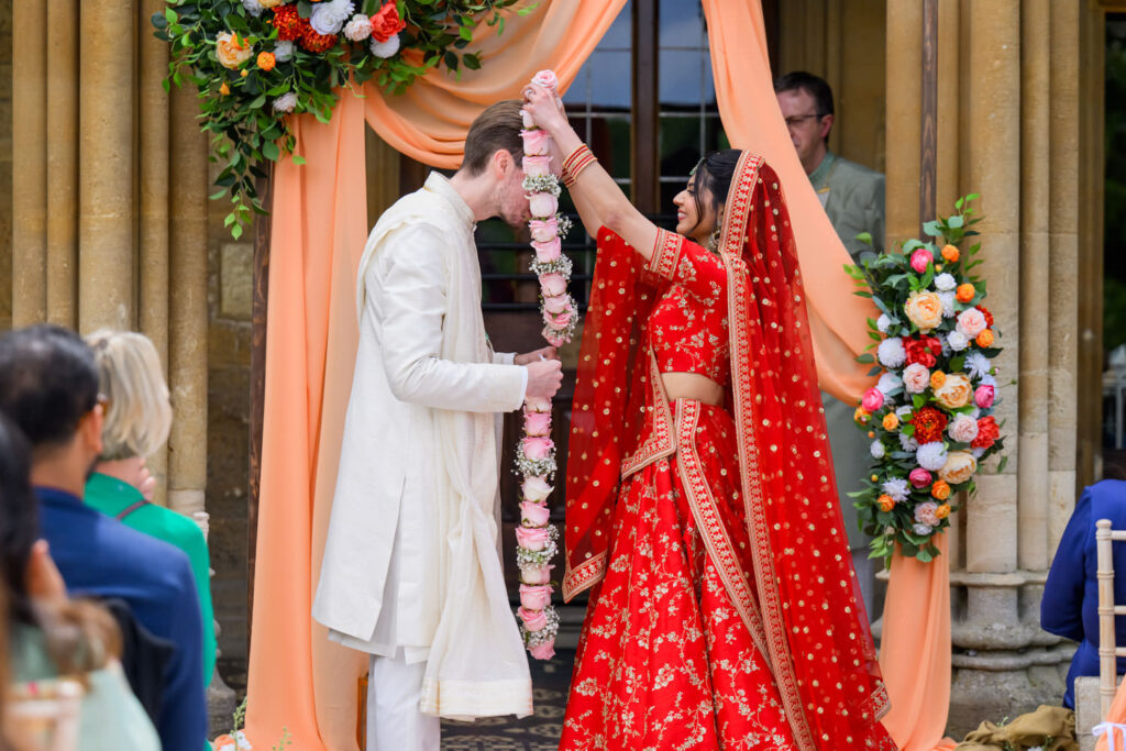 Bride placing a garland on the groom during their Manor by the Lake wedding ceremony.