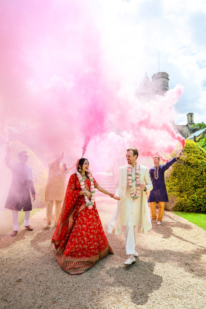 Newlyweds walking through pink smoke in the gardens at Manor by the Lake.