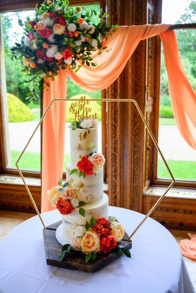 Elegant three-tier wedding cake with vibrant floral decorations photographed at Manor by the Lake.