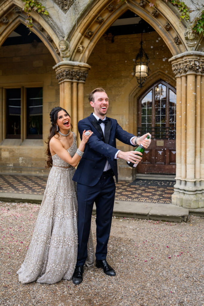 Bride and groom popping champagne in the courtyard during their wedding photography portraits in Cheltenham.