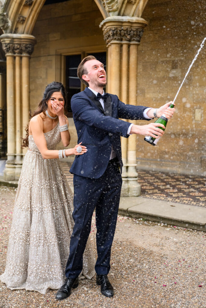 Bride and groom laughing as they spray champagne outside Manor by the Lake during relaxed wedding portraits.
