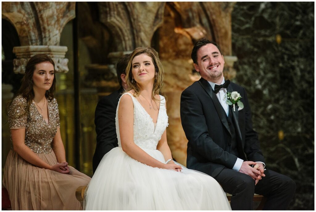 bride and groom sat down smiling during wedding ceremony at Farm Street Church
