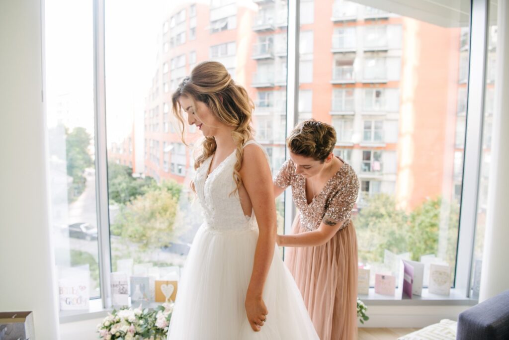 bridesmaid wearing pink helping to do up brides wedding dress