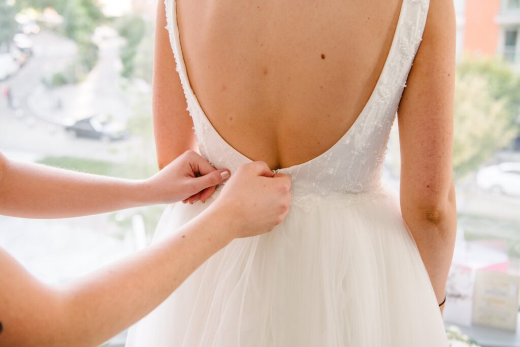 bridesmaid helping to do up the back of brides dress