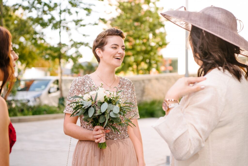 bridesmaid laughing whilst wearing pink glitter dress and holding flowers