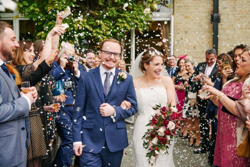 Happy bride and groom laughing whist friends and family throw confetti
