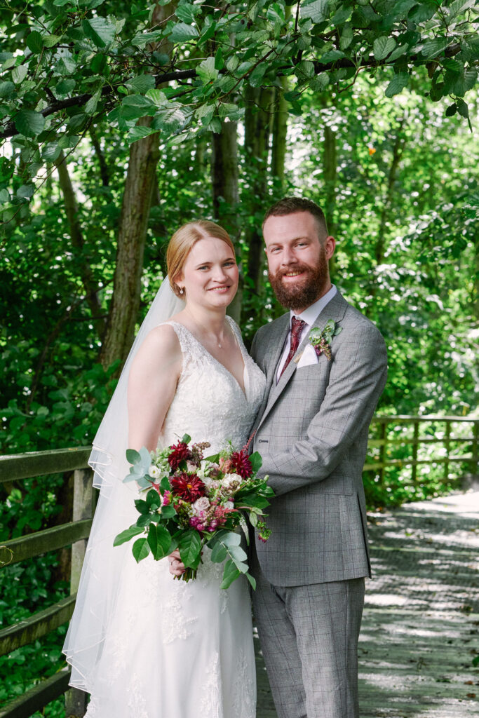 Bride and groom stood smiling together on a walkway under trees