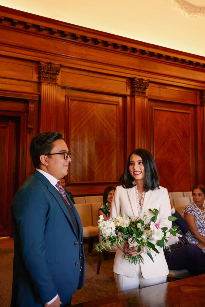 Bride wearing a white pantsuit smiling during intimate wedding ceremony