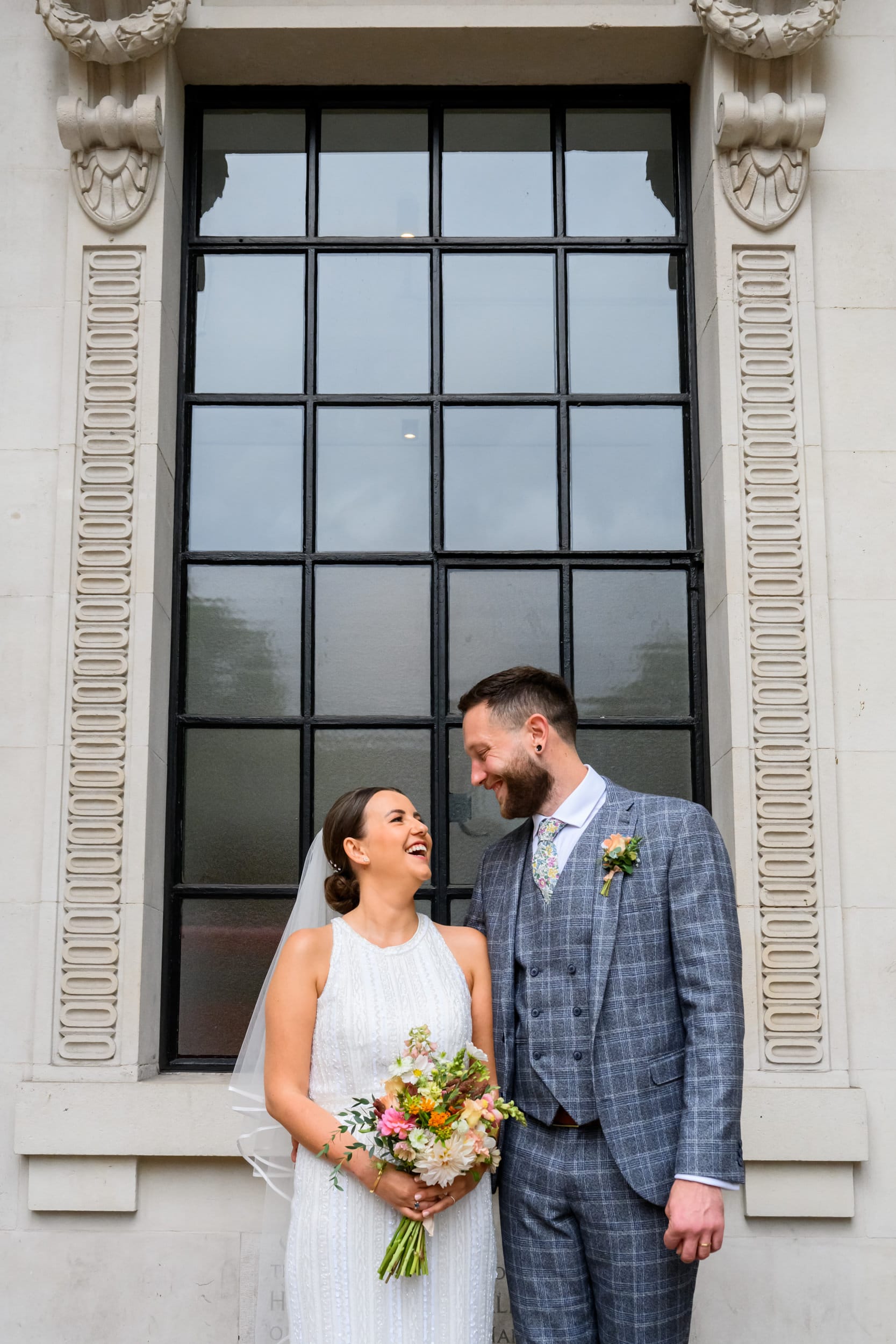 Marylebone Town Hall Wedding Photography happy bride and groom in front of black framed window during london wedding