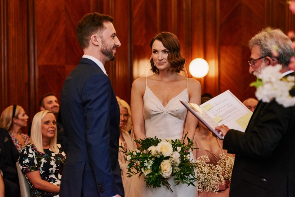Bride and groom smiling during their ceremony in the Westminster room at Old Marylebone Town Hall