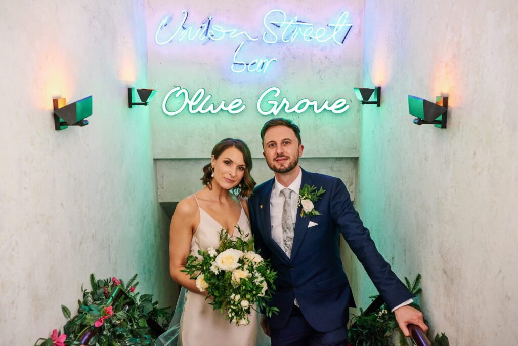 Wedding couple in front of the neon Olive Grove sign at Union Street Café