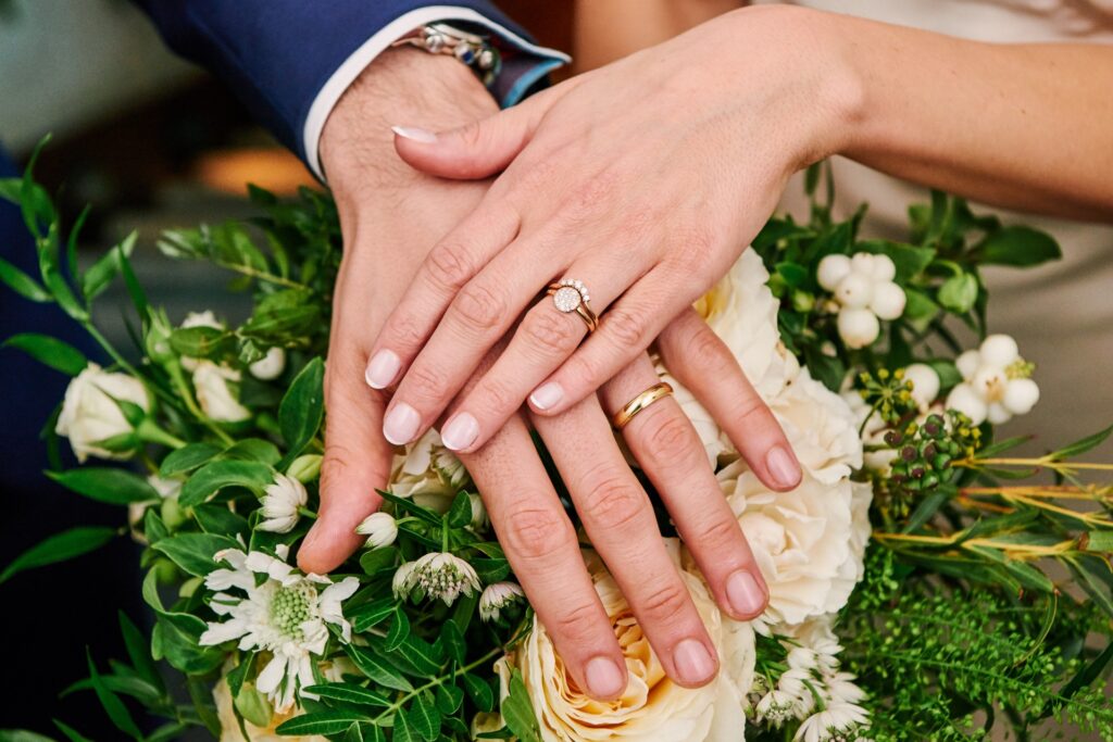 Bride and grooms hands on top of flowers showing wedding rings