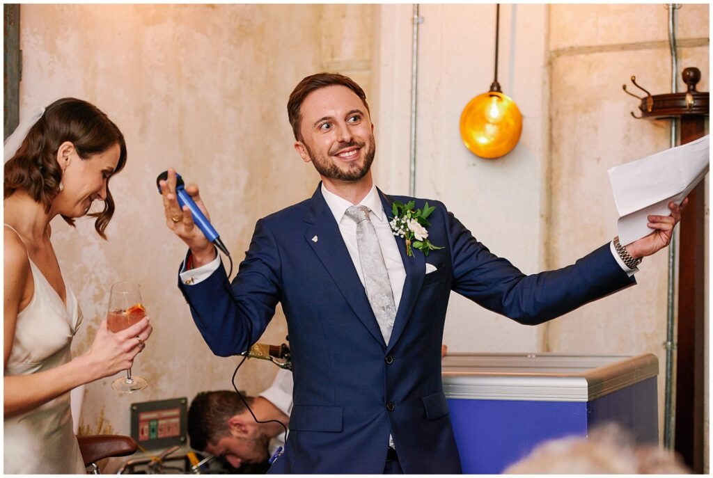 Groom giving a speech in front of a rustic wall at the Olive Grove