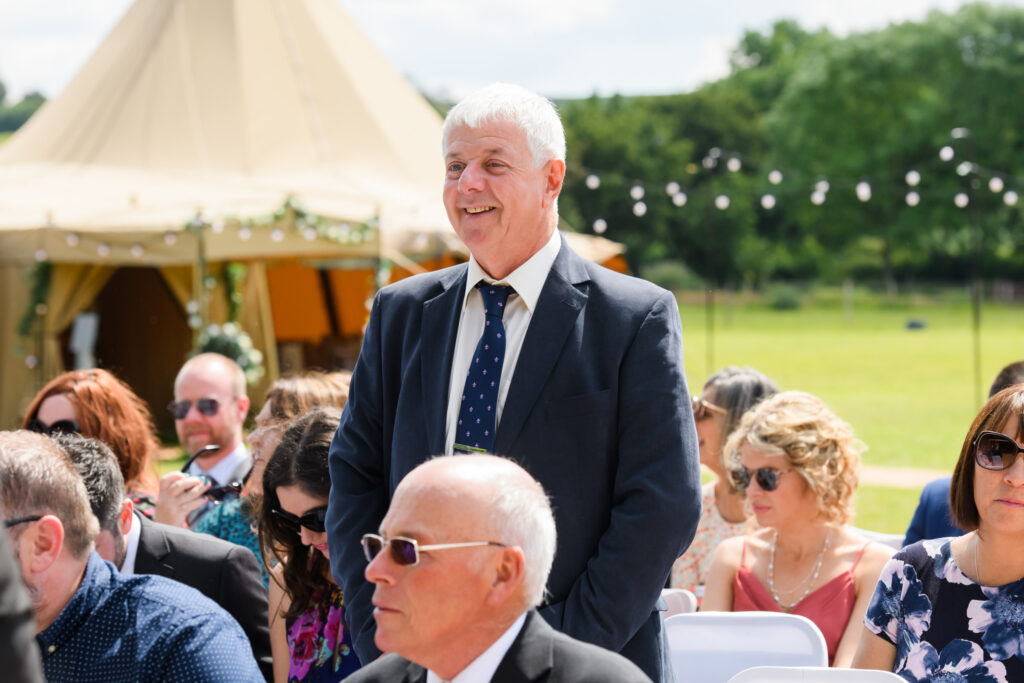happy male guest stood in front of tipi during outdoor wedding ceremony