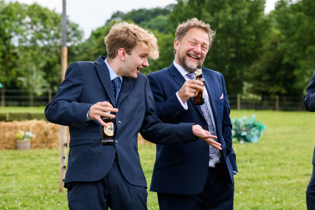 Two male wedding guests laughing and having fun during outdoor festival wedding