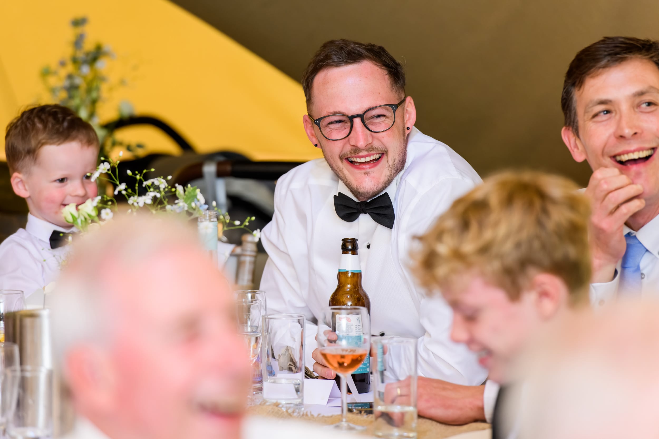 Candid photography featuring best man laughing whilst inside wedding tipi